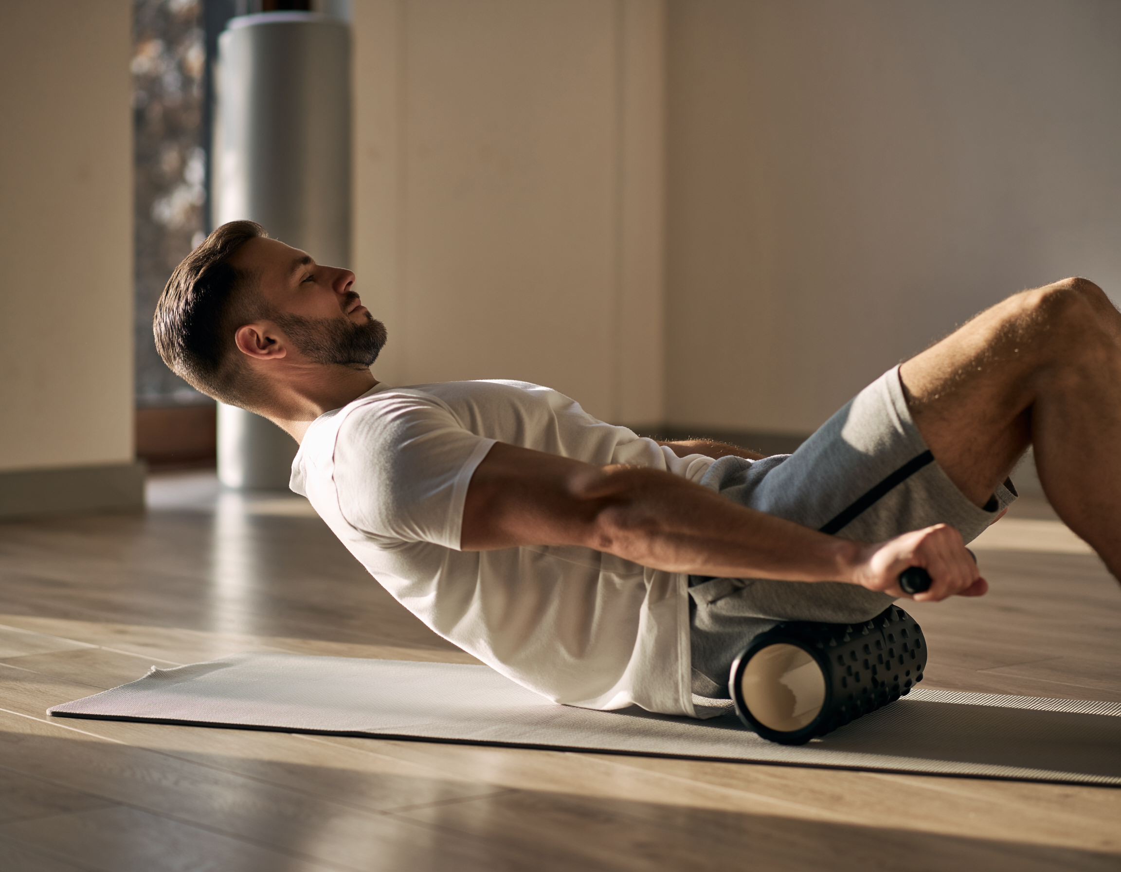 Mann führt auf einer Matte eine Übung mit der Faszienrolle durch – Beispiel aus der Faszientherapie zur Lockerung und Regeneration des Bindegewebes.